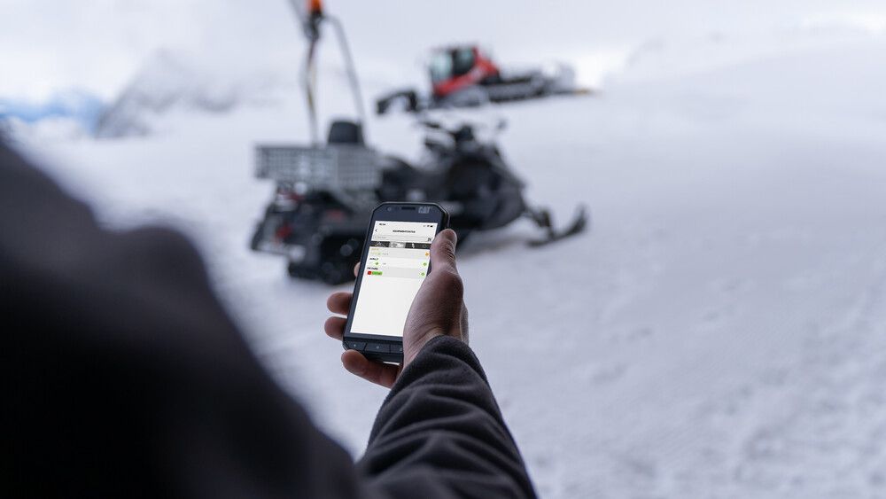 Eine Person bedient SNOWsat Maintain am Smartphone auf der Piste.