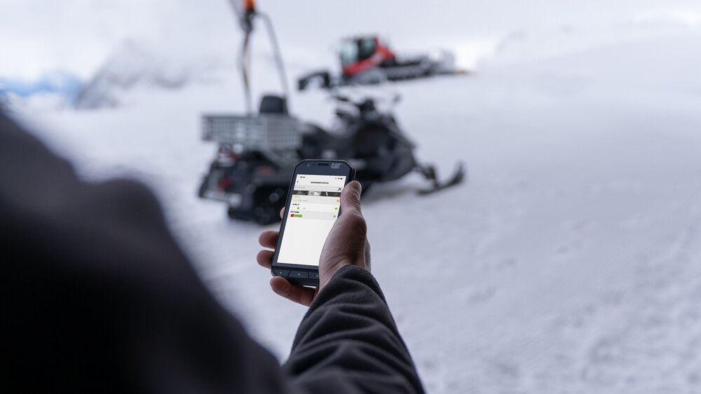 SNOWsat Maintain | Smartphone Eine Person bedient SNOWsat Maintain am Smartphone auf der Piste.