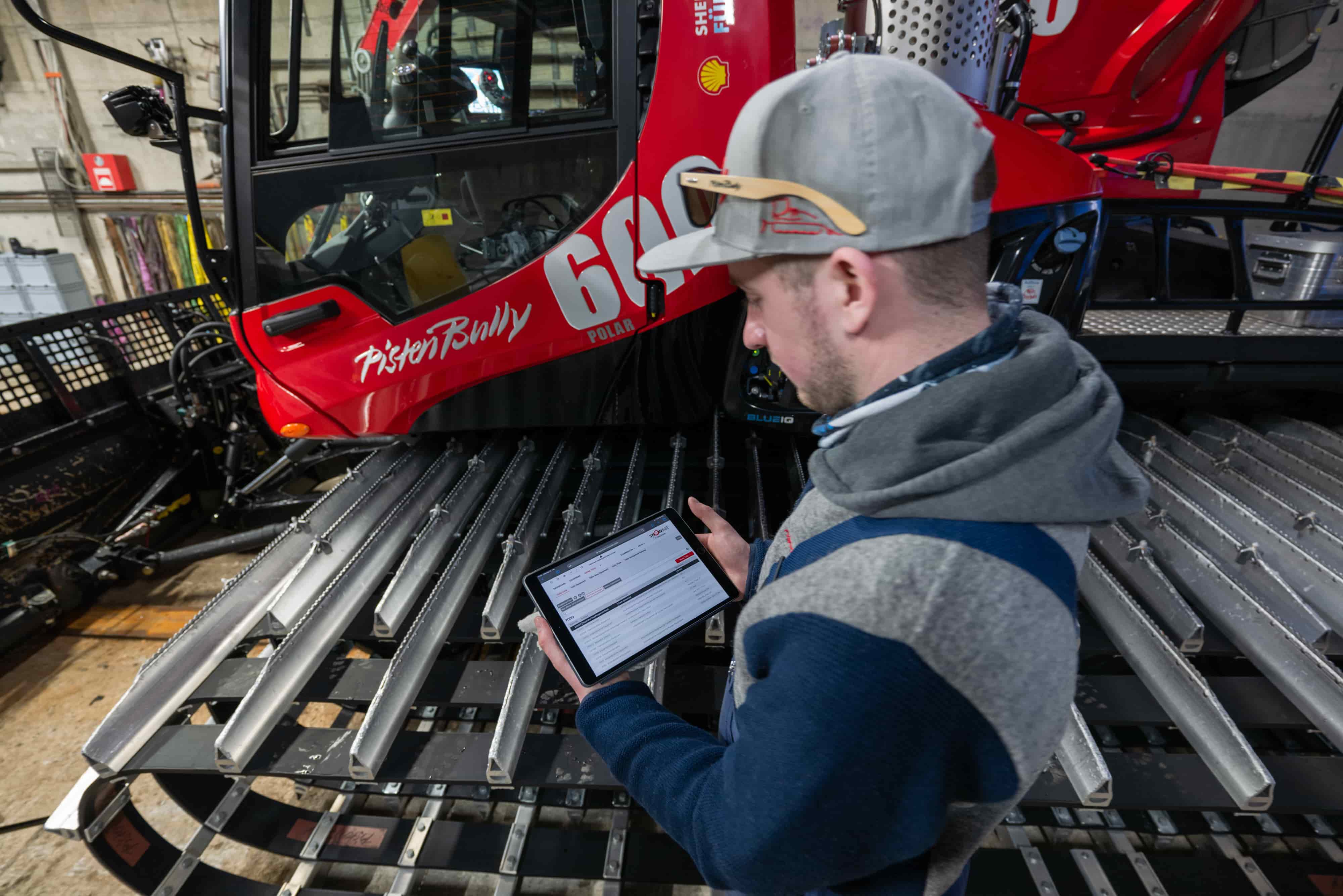 Dipendente dell'officina con SNOWsat Maintain sul tablet davanti a un PistenBully