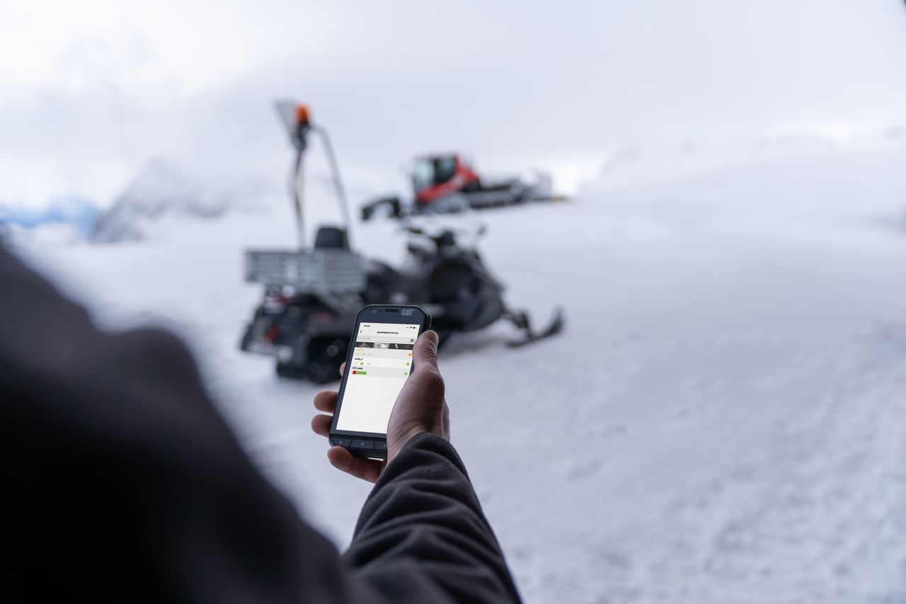 SNOWsat App auf dem Handy, im Hintergrund PistenBully