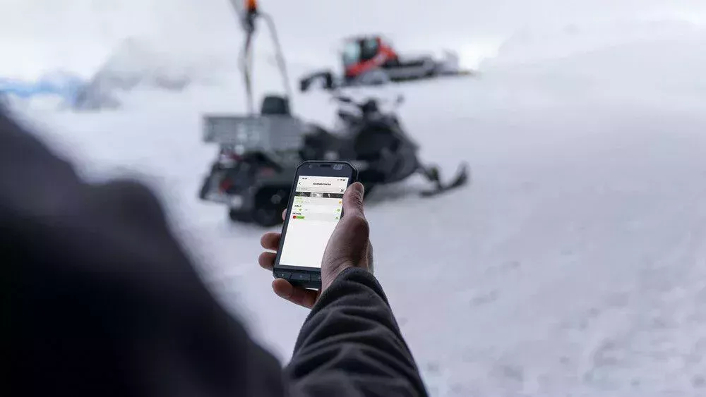 SNOWsat Maintain | Smartphone Eine Person bedient SNOWsat Maintain am Smartphone auf der Piste.
