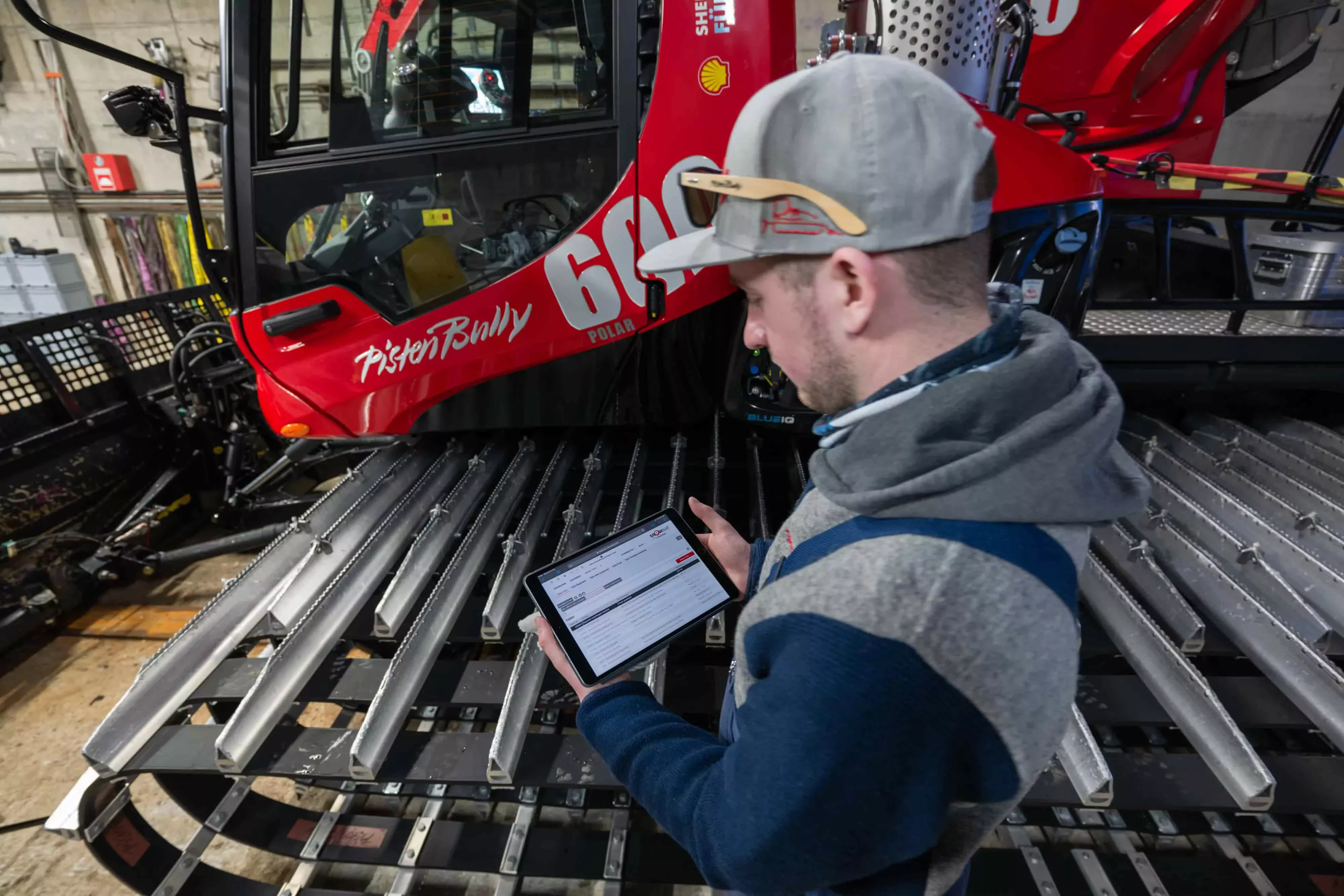 Werkstatt-Mitarbeiter mit SNOWsat Maintain auf dem Tablet vor einem PistenBully