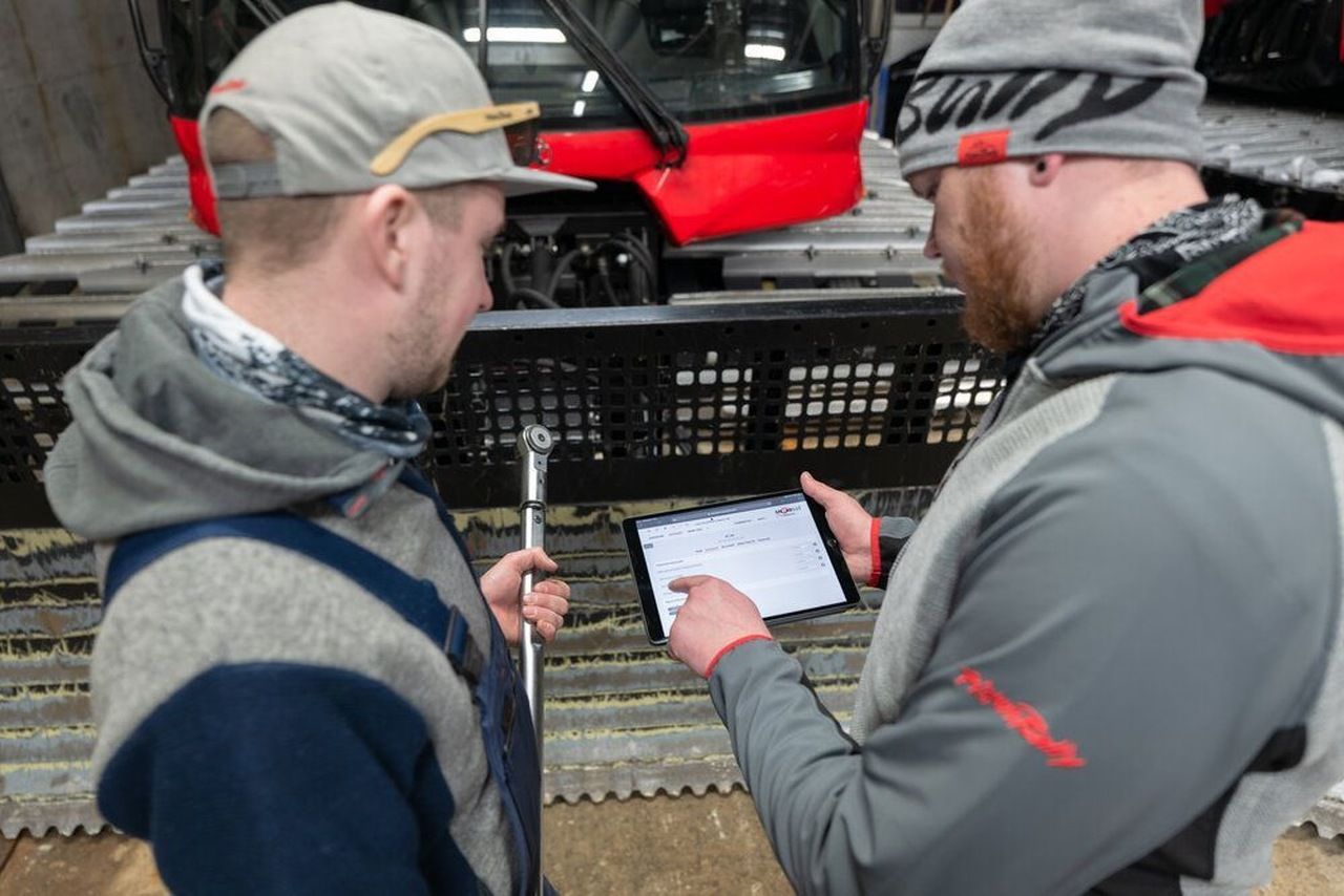 App SNOWsat sul tablet, un PistenBully sullo sfondo